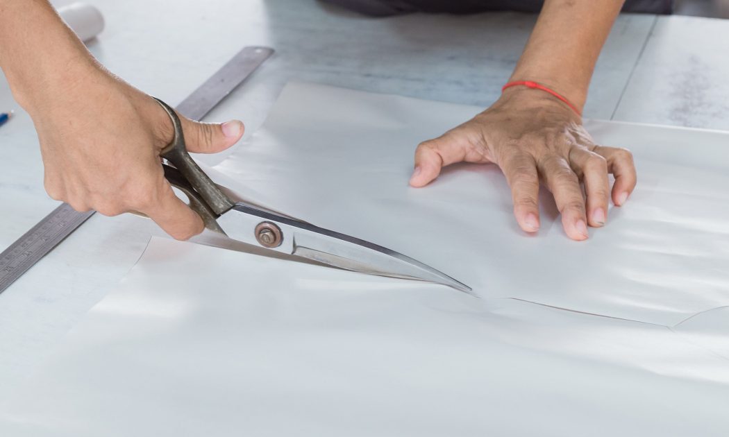 Pattern maker cutting a paper pattern with scissors